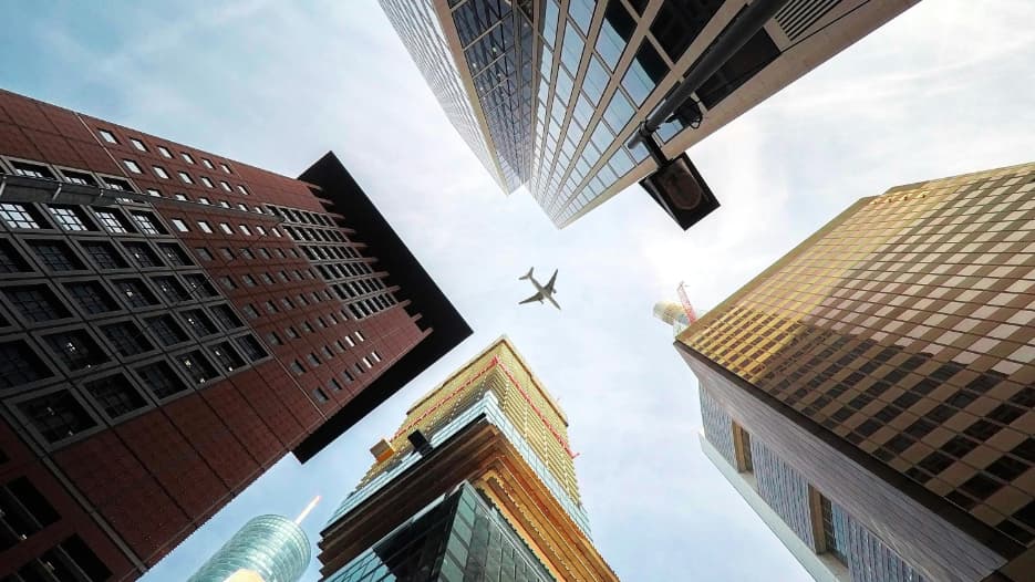 Blick nach oben: Wolkenkratzer und Flugzeug am Himmel.