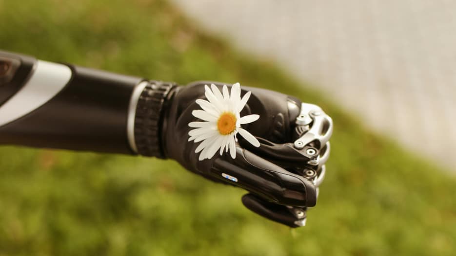 Roboterhand hält ein Gänseblümchen vor grünem Hintergrund