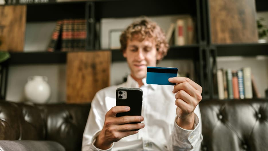 Person sitzt auf Ledersofa und hält Kreditkarte und Smartphone für Online-Banking